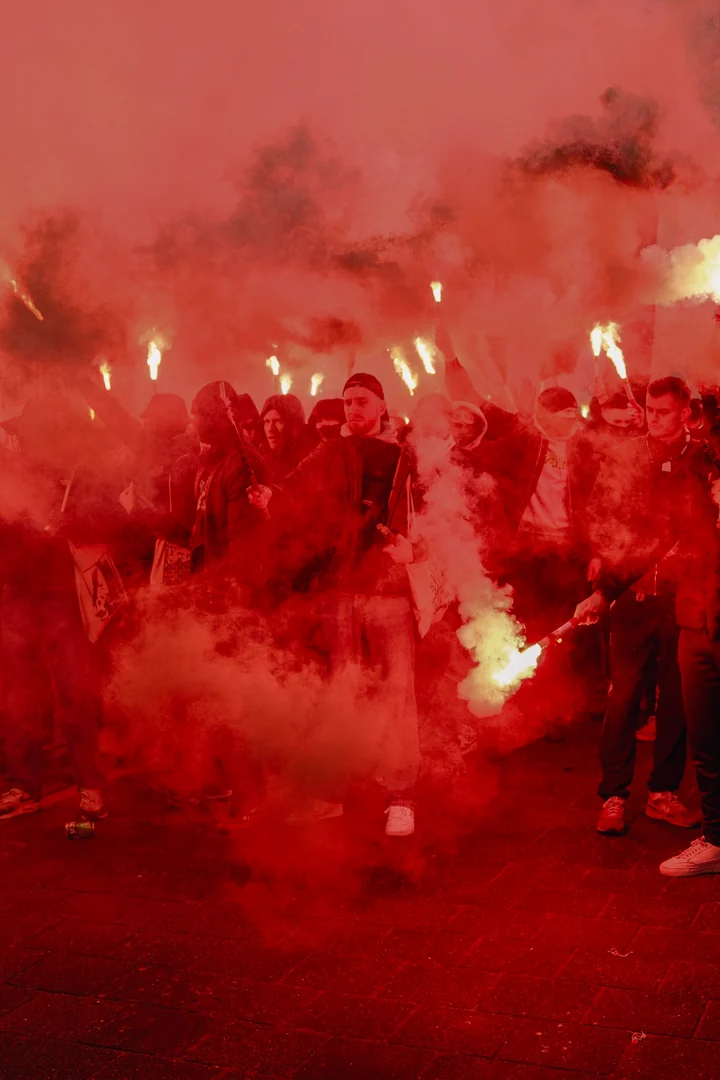 Supporters lopen door een dichte rode rookwolk met fakkels